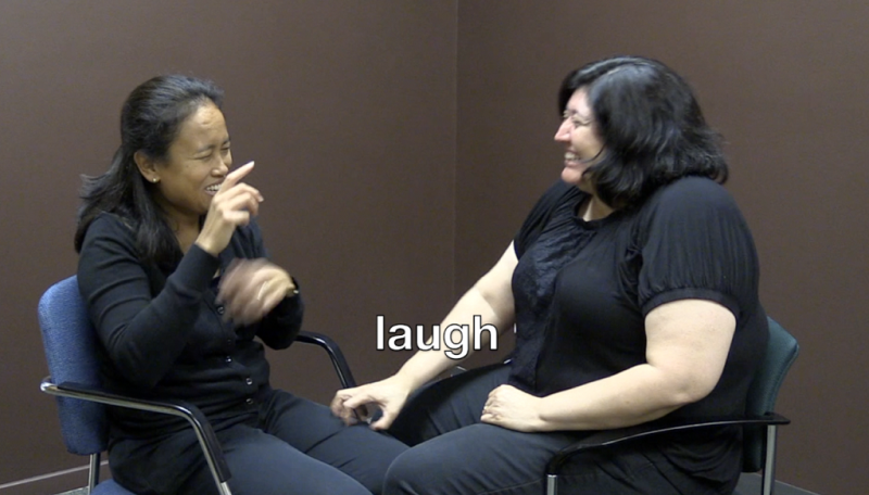 A woman signing while another woman touches the signing woman's thigh