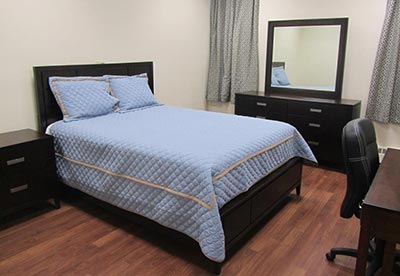 Helen Keller National Services dorm bedroom showcasing a bed with a blue bedspread, a dark brown nightstand, a dark brown dresser, and a mirror