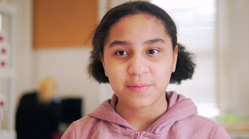 Young girl with her hair up in 2 buns wearing a pink sweater