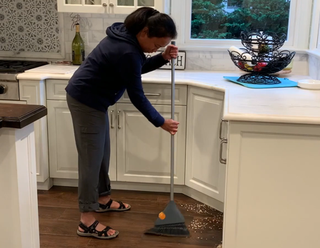 A woman sweeping a kitchen floor with a broom