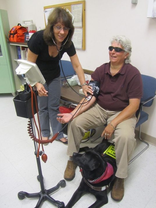 A woman checking another person's blood pressure. 