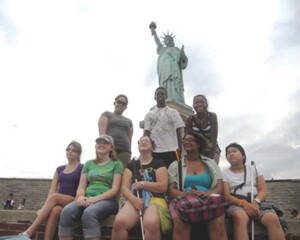 Group of young men and women sitting and standing in front of the Statue of Liberty
