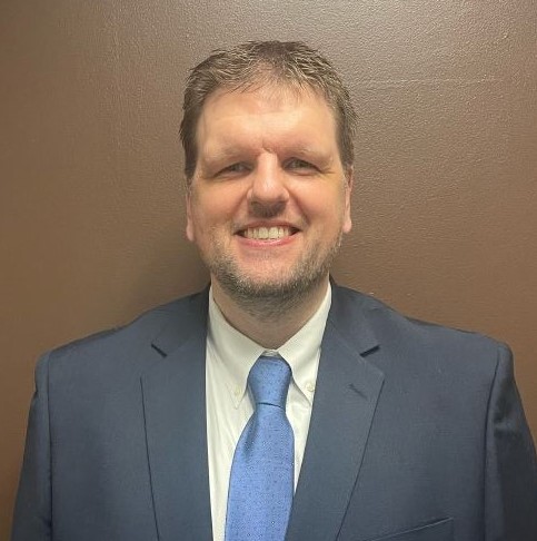 Headshot of a man wearing a suit and tie smiling into the camera