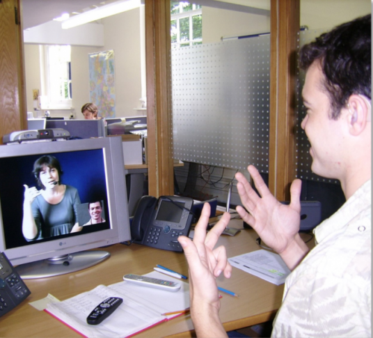 A man sitting at office desk signing with a woman on a computer video call