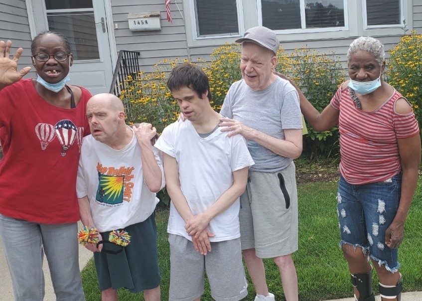 Group of 5 adults standing on a lawn in front of a house
