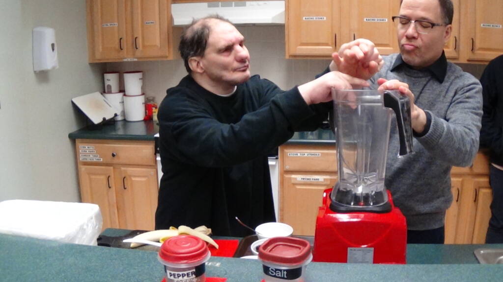 Two men touching a blender in a kitchen