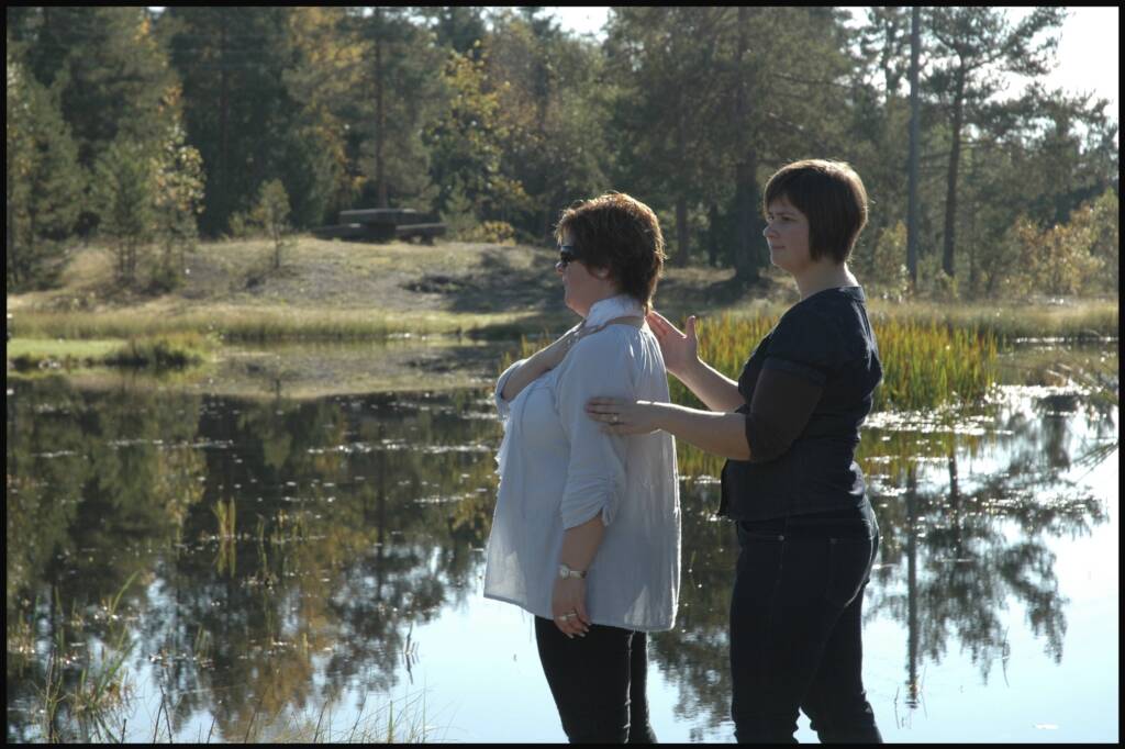 A woman touching another woman's arm and back in front of a body of water