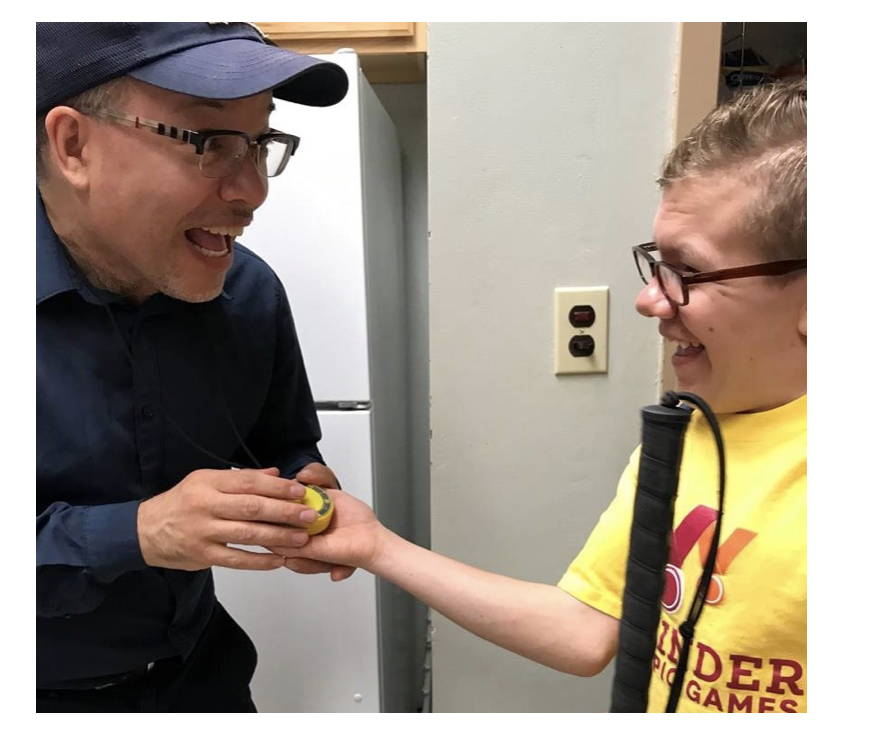 Two people holding a small yellow object while one of the people also holds a cane