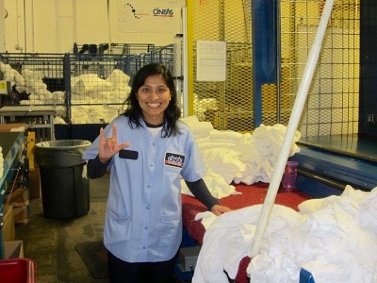A woman signing I Love You and wearing a work shirt while surrounded by piles of white towels