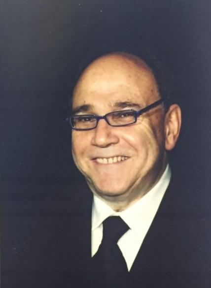 Lawrence Wizel smiling into the camera wearing a suit, a tie, and glasses