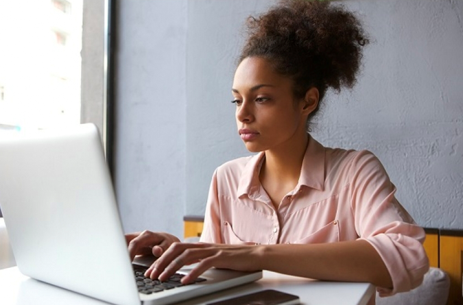 a dark skinned woman typing on a laptop