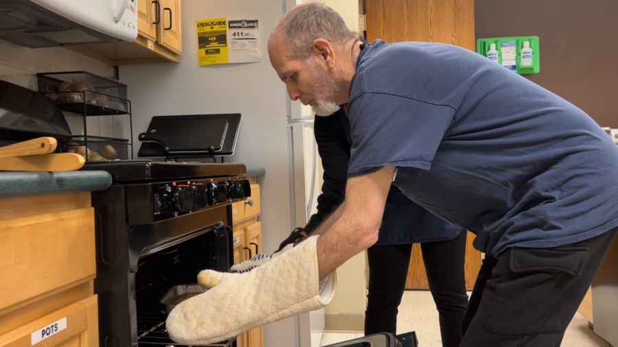 A man leaning over near an oven and wearing oven mits