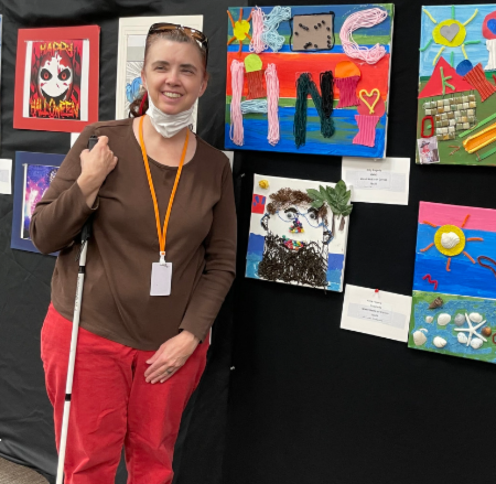A woman smiling next to her artwork at an art show