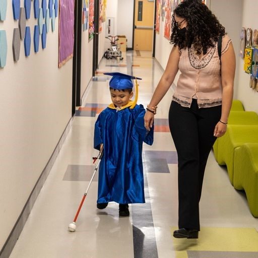 young boy holding a white cane in a hallway while holding a woman's wrist