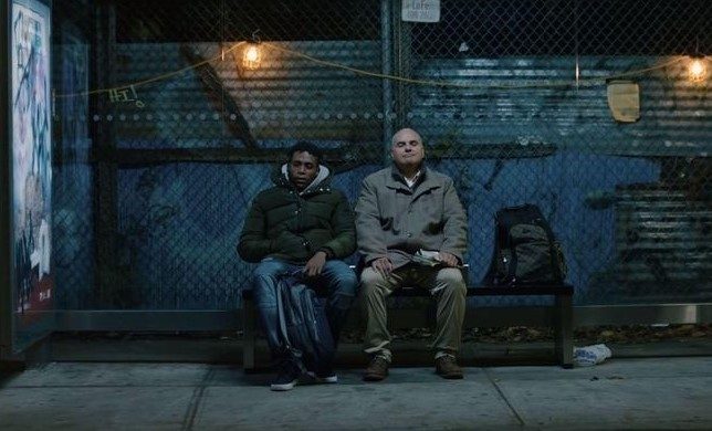 Two men sitting on a bench outside in the dark
