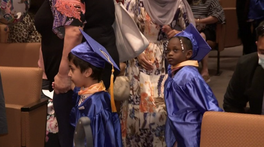Two preschool children wearing blue graduation caps and gowns