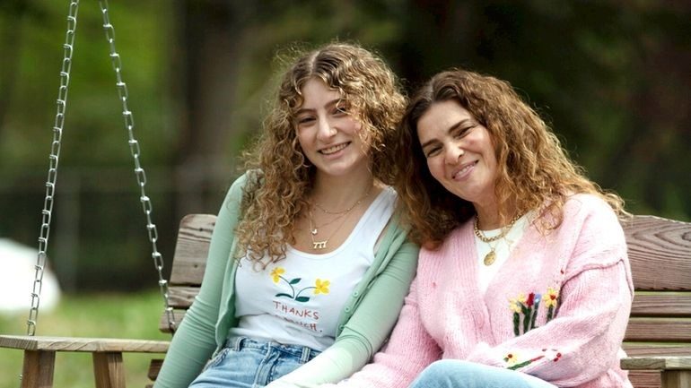 A teenage girl and a woman sitting close together on a porch swing outside and smiling