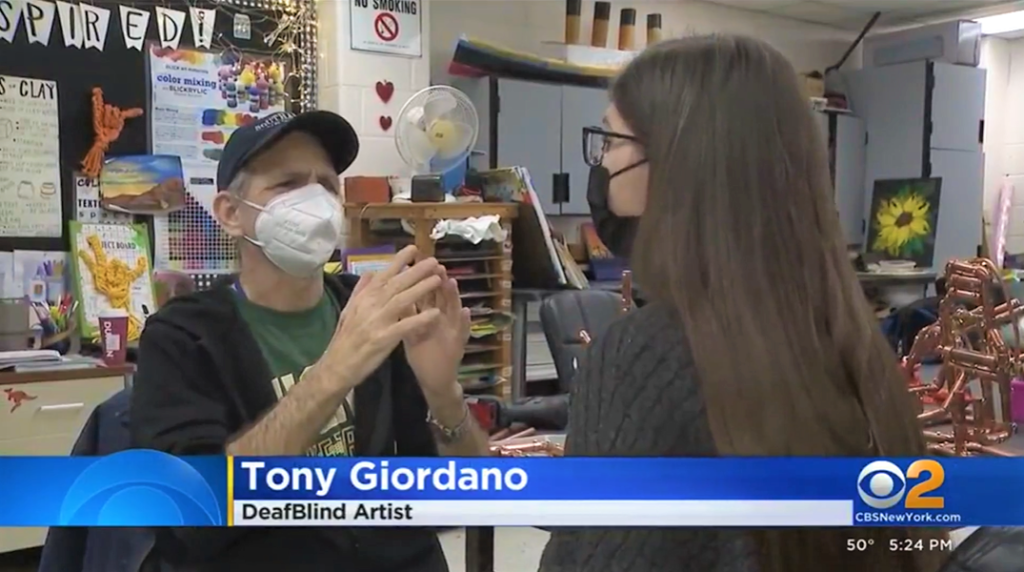 Tony Giordano signing to a CBS news reporter in the Helen Keller National Center art classroom