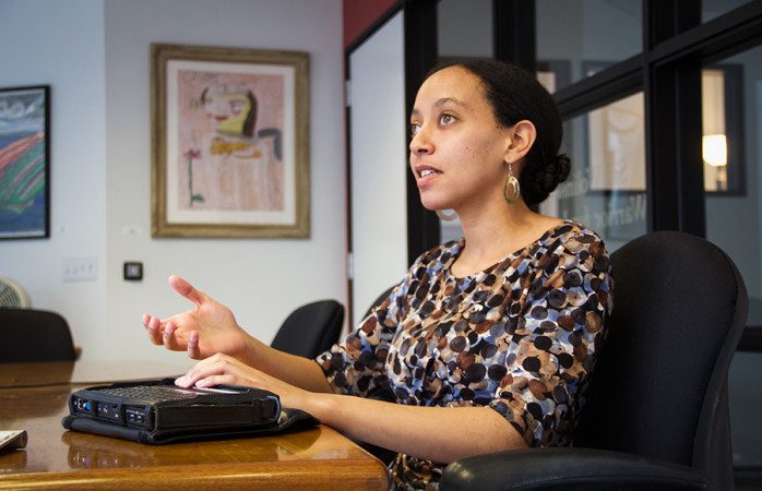 A woman sitting at a desk and touching an assistive technology device with her left hand