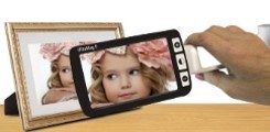 A black handheld magnifier being held in front of a picture frame. On the magnifier is an enlarged image of a photo of a young girl with a large light pink flower in her hair