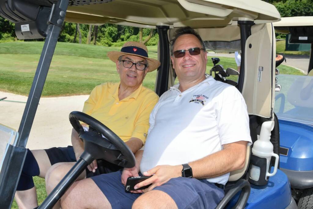 Joe Mancino and his son smiling and sitting in a golf cart outside