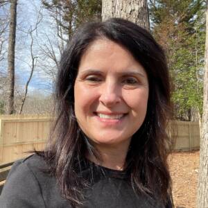 A white woman with dark hair smiling into the camera outside