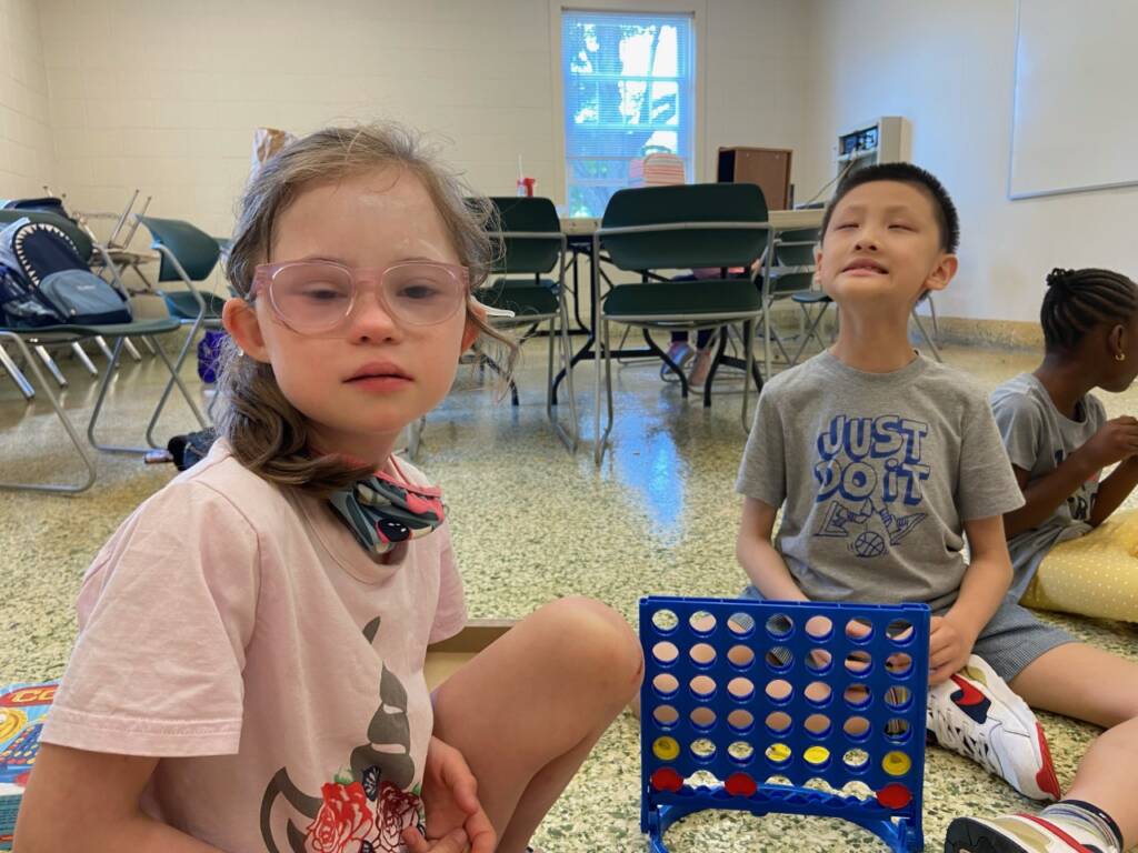 A girl and a boy playing Connect 4 on the floor of a room