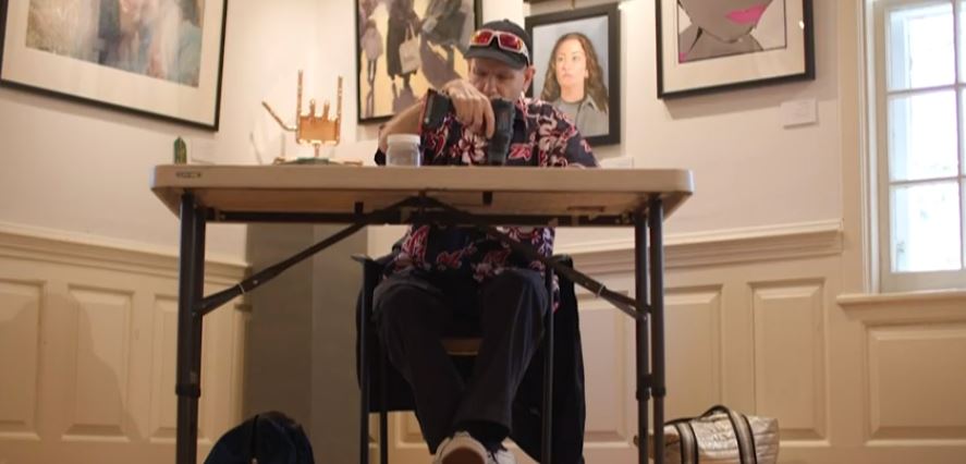 A DeafBlind man sitting at a table and using a drill to put together a copper sculpture at an art museum