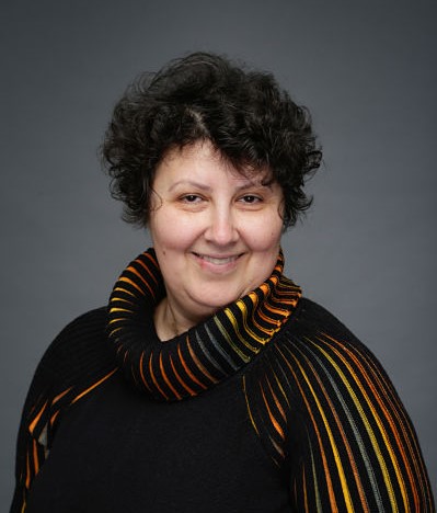 a woman with tan skin and short black curly hair smiling into the camera