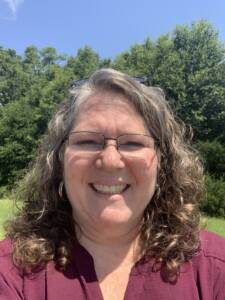 A woman with curly hair and glasses smiling into the camera outside