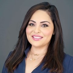 Head shot of a woman with light skin and long brown hair wearing a blue v-neck blouse.