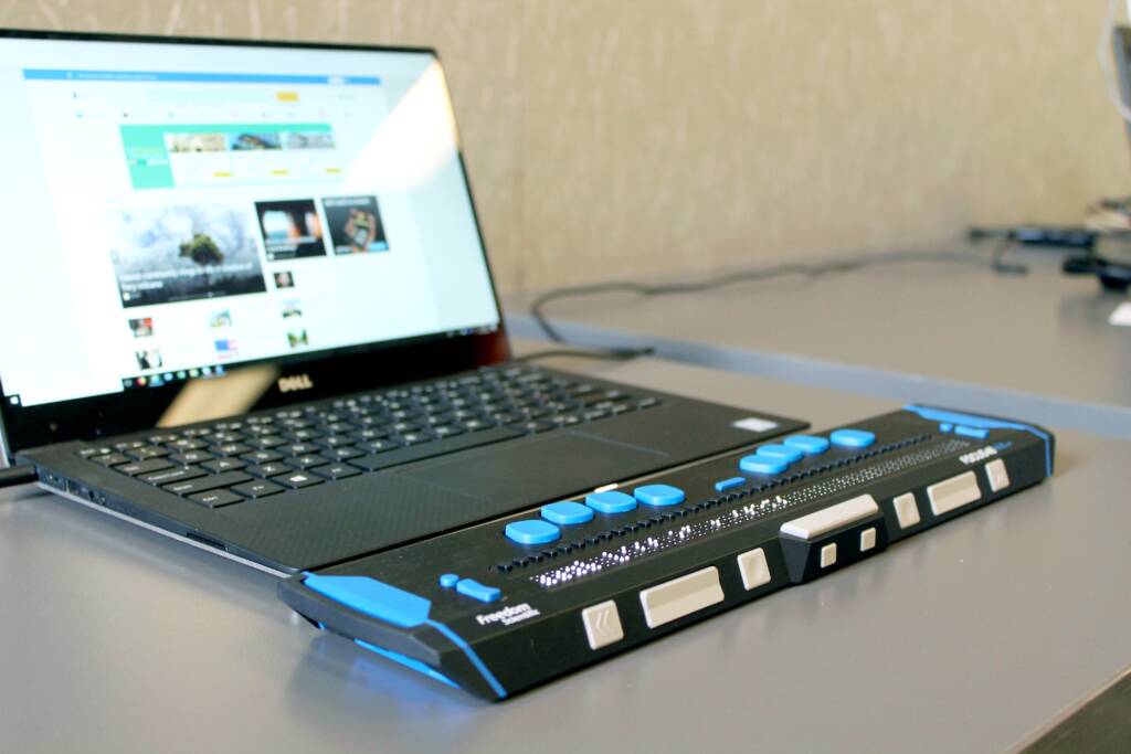 An open laptop and a braille display on a desk