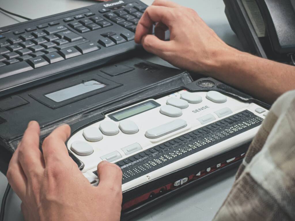 a person touching a braille display and a computer keyboard in front of it