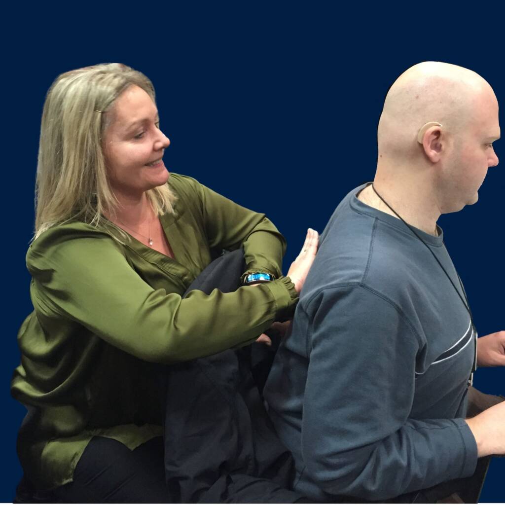 A woman communicating through haptics by putting her hands on the back of a DeafBlind man