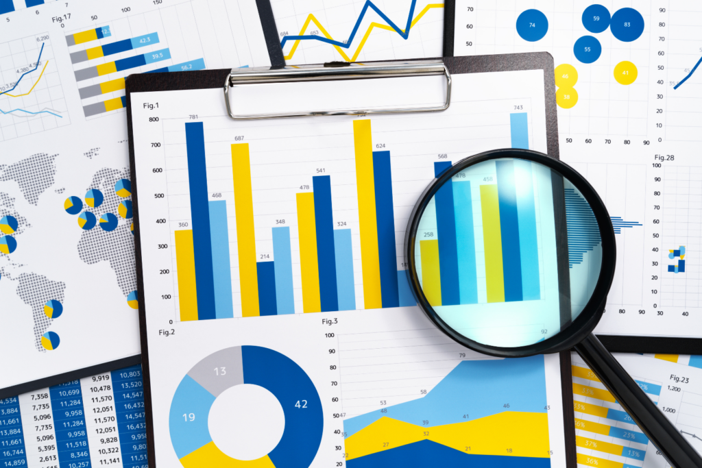 A magnifying glass sits on top of papers that have graphs and charts on them.