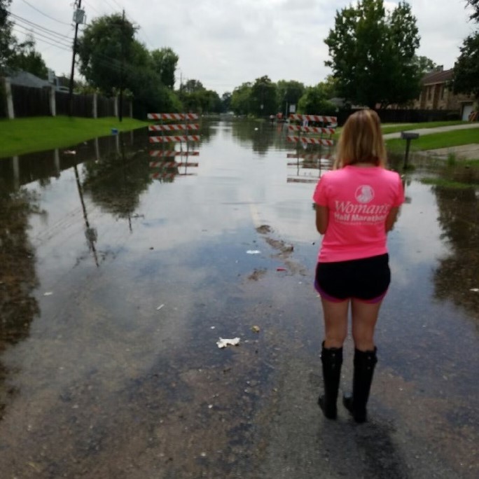 A woman with her back to the camera stands on a road that has become flooded with water