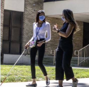 a woman walks with a white cane next to a woman outside