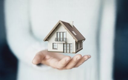 a small model of a home hovering on top of someone's hand