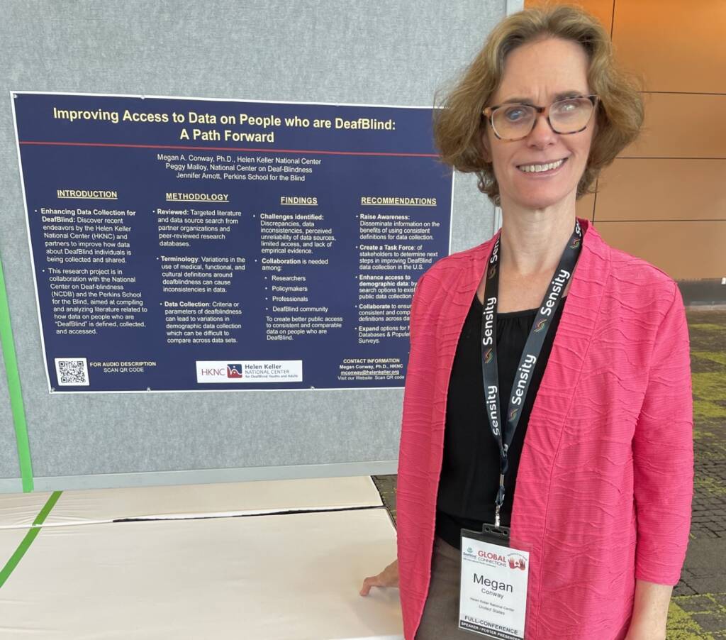 Dr. Megan Conway presenting her research poster at the DeafBlind International Conference. The poster is titled, " Improving Access to Data on People who are DeafBlind" and she is wearing a pink blazer.