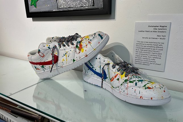 White Nike sneakers with rainbow paint splatters on them on display at an art museum