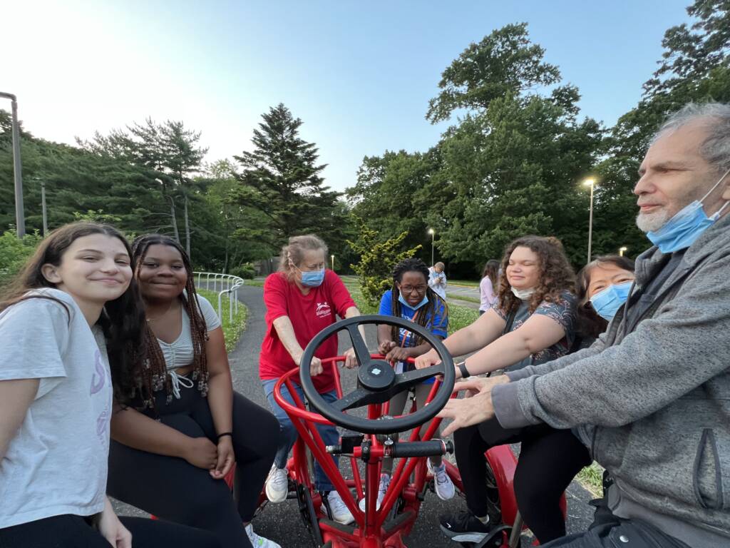 A group of kids and adults sitting on a conference bike outside