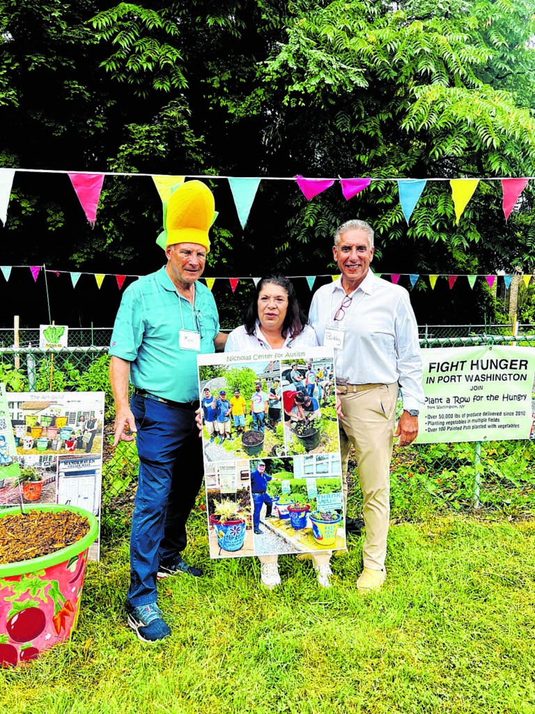 2 men and 1 woman standing outside in front of a garden while the woman holds a large poster that says "Nicholas Center for Autism" at the top and has photos of people gardening on it.