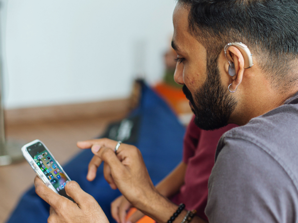 A man wearing a hearing aid holds an iPhone