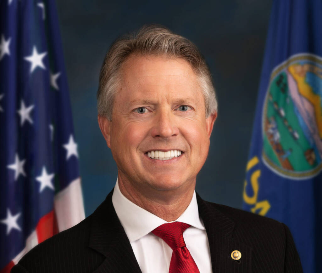 Senator Roger Marshall wearing a suit and tie and smiling into the camera. He's in front of an American flag and a Kansas flag