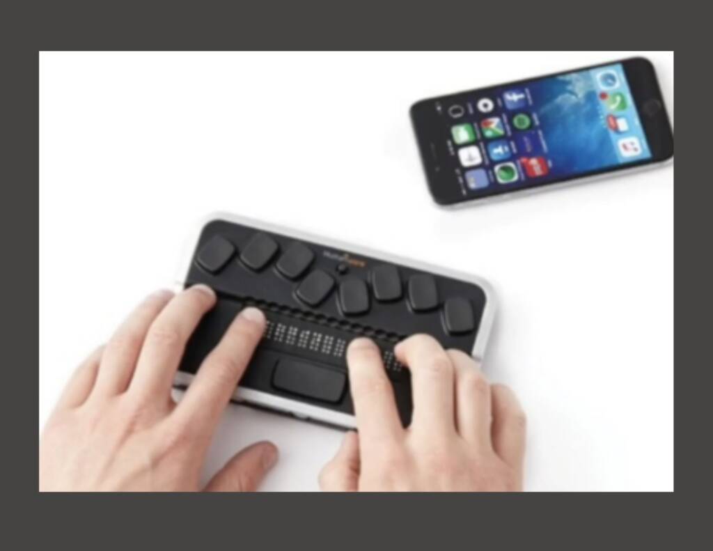 Person's hands touching a braille display near an iPhone