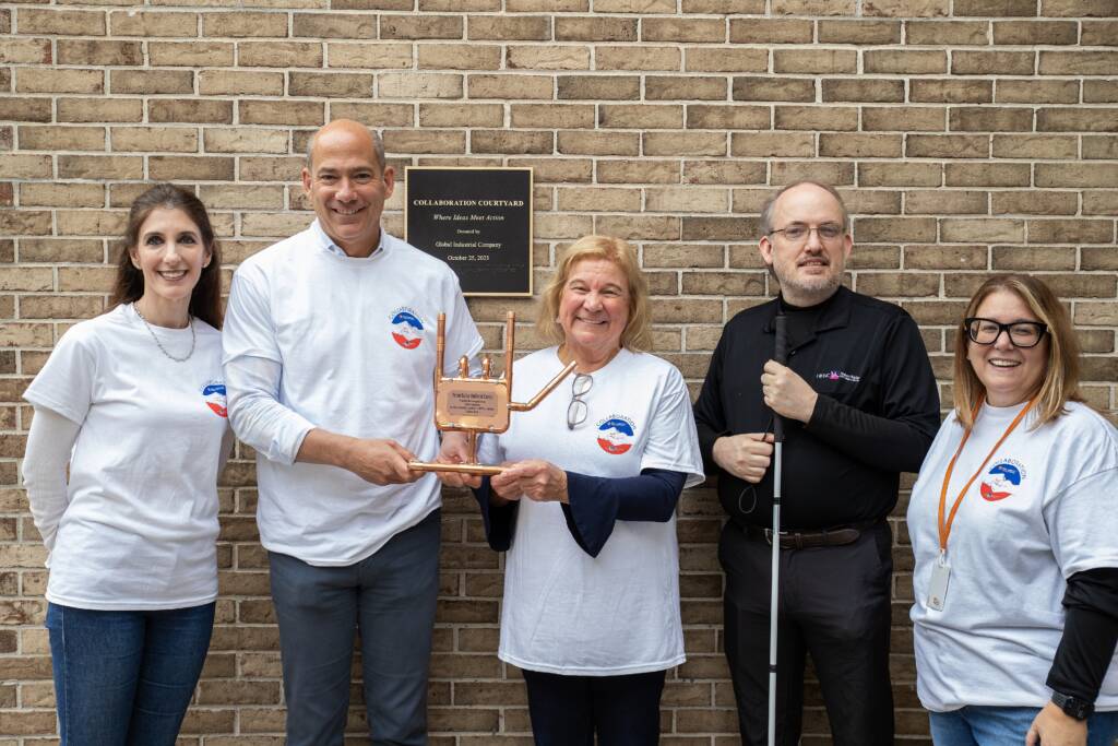 5 people standing next to each other and smiling while 2 of them hold an "I love you" sign sculpture.