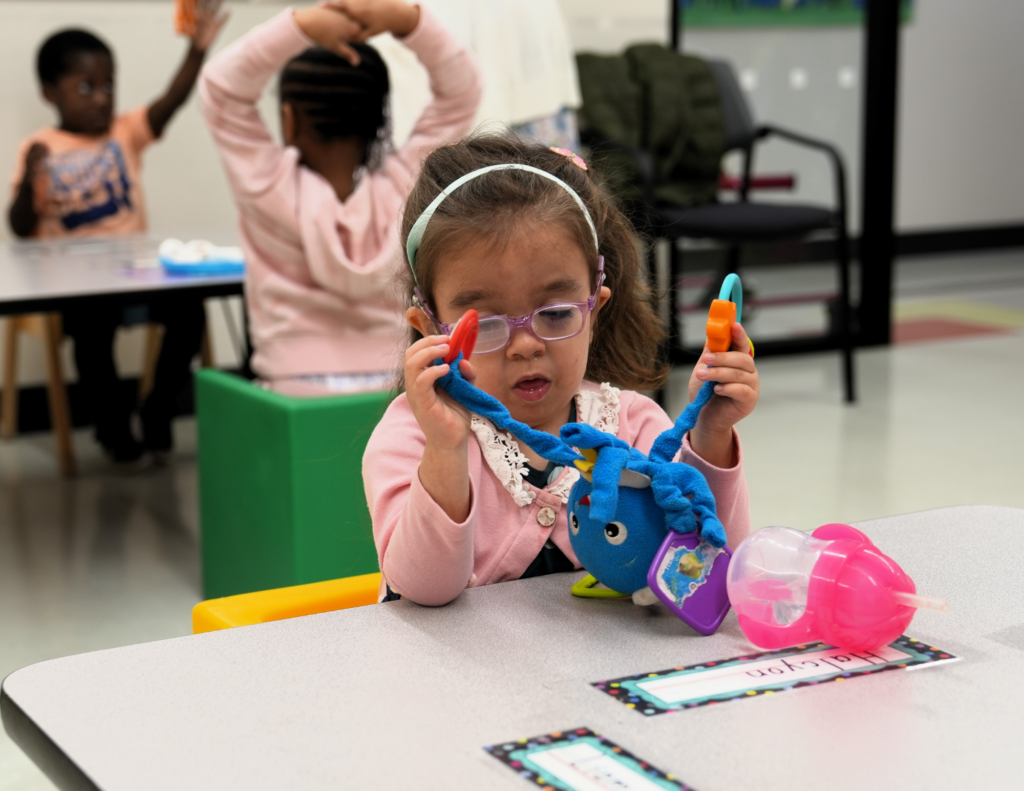 a young girl plays with a blue plush toy while sitting at a desk