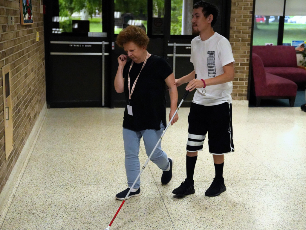 A boy holding a white cane in his left hand and the arm of the woman next to him in his right hand