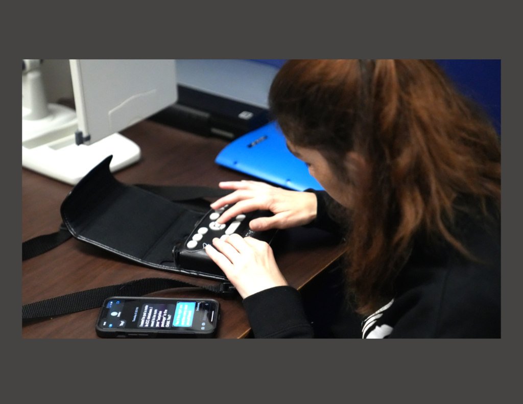 A woman using a braille display next to an iphone with a screen showing her iMessages on it