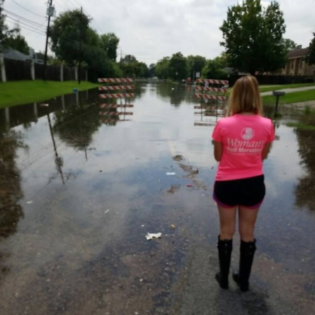 A woman with her back to the camera stands on a road that has become flooded with water